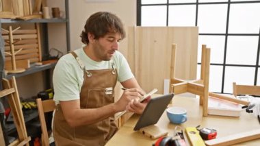 Yakışıklı sakallı adam, ahşap mobilyalarla dolu, parlak bir marangozluk atölyesindeki tablete notlar alıyor..