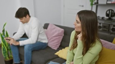 Gündelik giysiler içindeki bir kadın ve erkek modern bir oturma odasında ayrı otururlar ve ilişkilerinde mesafelerini gösterirler..