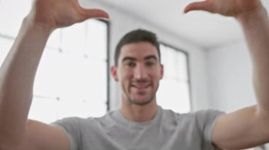 Yakışıklı İspanyol adam modern bir oturma odasında gülümsüyor. Büyük pencereleri ve minimalist dekorasyonu var.