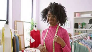 Renkli bir atölyede duran gülümseyen siyah kadın terzi.