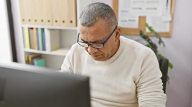 Ofisteki stresli İspanyol olgun adam bilgisayar başında çalışırken gözlüğünü çıkarıyor..