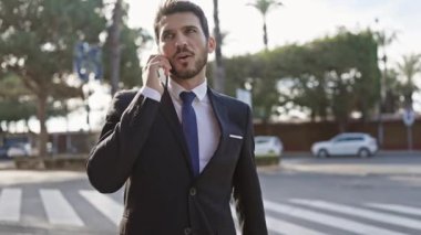Takım elbiseli yakışıklı genç adam şehir caddesinde telefonla konuşuyor..