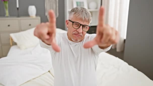 笑顔の灰色の髪のミドルエイジング男性は 手と指でフレームを作成し カメラの視点で彼の寝室のビューをキャプチャ — ストック動画