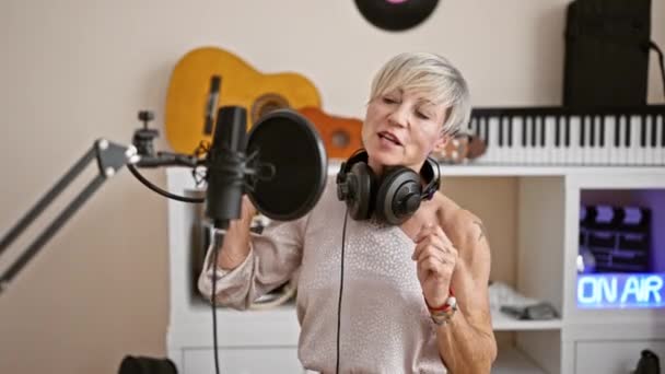 成熟した女性は 音楽スタジオのインテリアでヘッドフォンで歌い 喜びと情熱を表示します — ストック動画