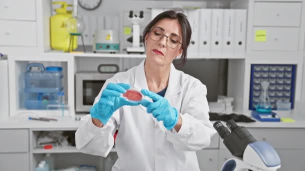 一位穿着实验室外套的专心致志的女科学家在现代实验室环境中对样品进行了检查 描绘了专业精神和对细节的关注 — 图库视频影像