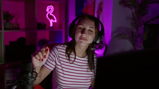 夜のネオンライトゲームルームで音楽を楽しんでいるヘッドフォンを持つ若い女性 — ストック動画