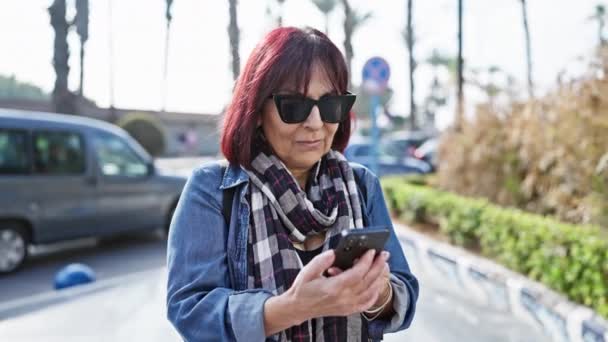 晴れた都市の通りでスマートフォンを使用して 赤い髪の成熟した女性 — ストック動画