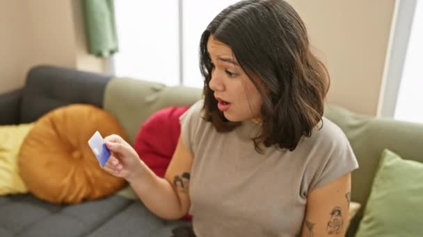 パニックになった若いヒスパニックの女性は ショックと恐怖で口を覆い 自宅でソファーに座っているクレジットカードの間違いを発見します — ストック動画