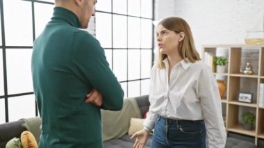 Bir erkek ve kadın, sıcak bir oturma odası ortamında endişe ifadeleriyle ciddi bir tartışma önerisinde bulunuyorlar..