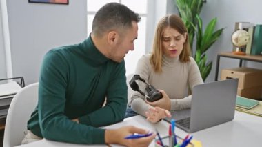 Ofisteki kadın ve erkek arızalı kulaklıklarla kafası karışmış. Bu da iş yerinde teknik bir sorun olduğunu gösteriyor..