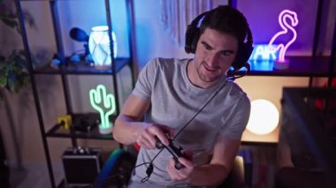 Genç bir adam geceleri loş ışıklı bir oyun odasında video oyunları oynuyor. Odaklanmış ve eğlenmiş görünüyor..