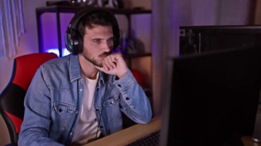 Kulaklıklı, karanlık bir oyun odasında bilgisayar ekranına bakan odaklanmış bir adam..