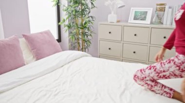 Uzun saçlı genç bir Güney Asyalı kadın rahat bir yatak odasında pijama giyiyor, evinde huzur ve sükuneti simgeliyor..