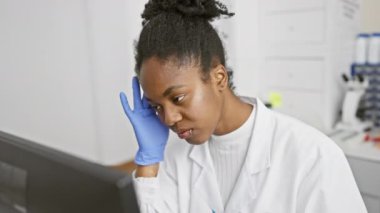 Odaklanmış Afrikalı bir bilim adamı laboratuvar ortamında eldiven ve laboratuvar önlüğü giymiş bir bilgisayardaki verileri inceliyor..
