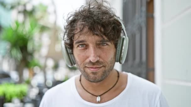 Cheerful Man Wearing Headphones Stands Smiling Sunny Urban Street Embodying — Stock Video
