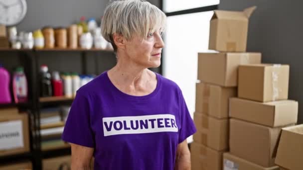 寄付箱や物資に囲まれた倉庫で微笑む成熟した女性ボランティア 積極性とコミュニティサービスを示す — ストック動画