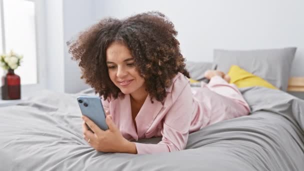 Heyecanlı Kıvırcık Saçlı Yatakta Uzanmış Rahat Yatak Odasındaki Akıllı Telefonuyla — Stok video