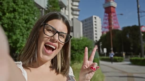鮮やかなスナップショット 東京でメガネをかけた美しいヒスパニックの女性 セルフィーのための平和のサインを笑い — ストック動画