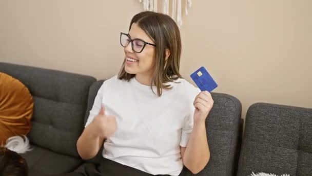 ジョイフルな若いヒスパニックの女性は 自信を持ってクレジットカードをオフに示す親指で指摘します 風変わりな家のインテリア 彼女の顔の美しい笑顔は 信頼と陽気さを除いて 金融について楽観的 — ストック動画