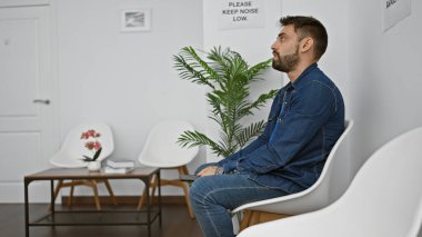 Yakışıklı, İspanyol asıllı, bekleme odasında dinlenen, akıllı telefon ekranına dalmış, gelişigüzel mesajlar yazan bir erkek. Kapalı arka planda rahatlama ve konsantrasyon portresi.