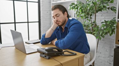 Genç İspanyol iş adamı ofiste dizüstü bilgisayar kullanıyor.