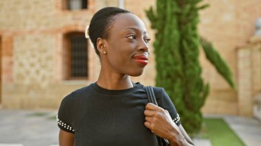 Kendine güvenen Afrikalı Amerikalı kadın yeşil parkta kahkahalarla eğleniyor. Yan tarafa bakarken mutluluğun bir portresi.