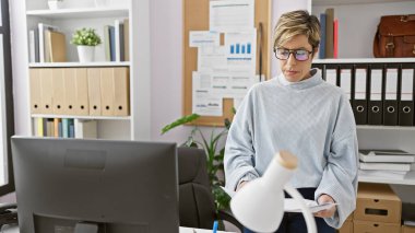 Profesyonel bir kadın, dosyalarla ve bilgisayarla dolu ofisindeki belgeleri inceliyor..