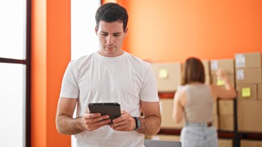 İki işçi adam ve kadın dokunmatik ped kullanarak iş yerindeki paketleri kontrol ediyorlar.