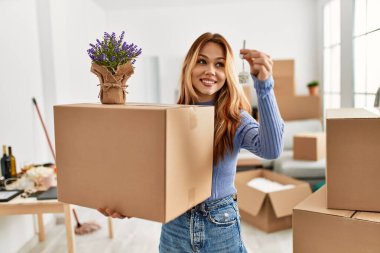 Beyaz kadın gülümsüyor. Yeni evinde kendine güveni olan lavanta bitkisi ve anahtar taşıyan bir paket taşıyor.