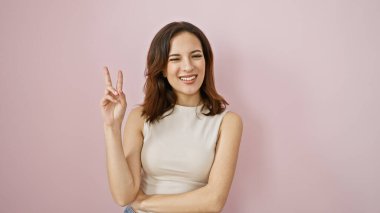 Gülümseyen genç İspanyol kadın pembe izole bir arka plana barış işareti yapıyor..