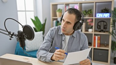 Handsome man working with microphone and headphones in modern radio station studio. clipart