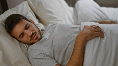 Sıcak bir yatak odasında beyaz bir yatak örtüsünün üzerinde huzur içinde dinlenen genç bir İspanyol..