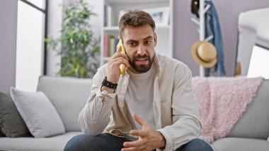 Genç İspanyol adam akıllı telefondan konuşuyor. Evdeki kanepede oturuyor.