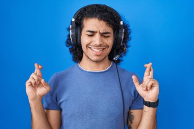 Kıvırcık saçlı İspanyol adam kulaklık takıp müzik dinliyor. Umut ve gözlerin kapalı bir şekilde gülümseyerek işaret ediyor. Şans ve batıl inançlar. 