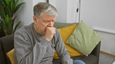 Düşünceli olgun bir adam evde oturur, rahat bir oturma odasındaki kanepede derin derin düşünür..