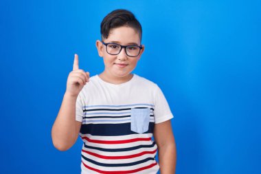 Mavi arka planda duran genç İspanyol çocuk bir numarayı gösterip işaret ederken kendinden emin ve mutlu gülümsüyor.. 
