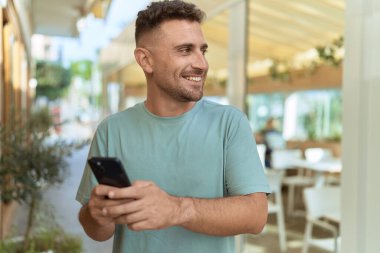 Young hispanic man smiling confident using smartphone at coffee shop terrace