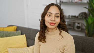 Modern bir oturma odasında rahat bir şekilde poz veren gülümseyen, melez bir kadının portresi..