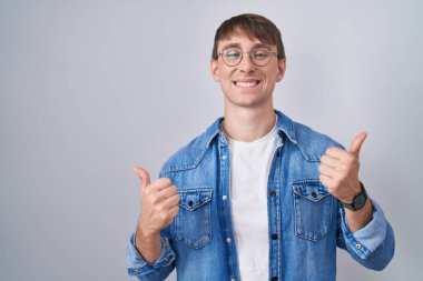 Beyaz, sarışın, gözlüklü, başarı işareti takan, elinde olumlu bir jest yapan, gülümseyen ve mutlu bir adam. Neşeli ifade ve kazanan jest. 