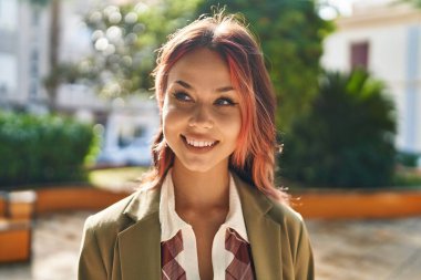 Beyaz bir kadın gülümsüyor parkın kenarına bakıyor.