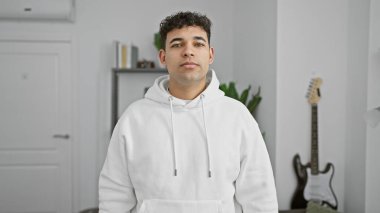 Modern bir salonda gitar çalan kapüşonlu sakallı yakışıklı bir genç..