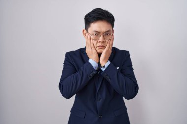 Asyalı genç adam iş elbisesi giyiyor ve kravat takıyor. Yorgun eller yüzünü kapatıyor. Depresyon ve üzüntü yaşıyor. 