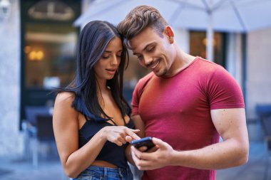 Kadın ve erkek kahve dükkanının terasında akıllı telefon kullanarak gülümsüyor.