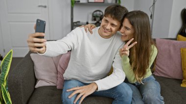 Bir erkek ve bir kadın sıcak bir oturma odasında selfie çektirmek için sarılır, sevgi ve mutluluk saçar..
