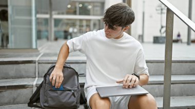 Havalı genç İspanyol öğrenci üniversite merdivenlerinde takılıyor, telefon elinde, ciddi bir çalışma seansından sonra rahatlamış, dizüstü bilgisayarı sırt çantasında ezmemeye dikkat ediyor.