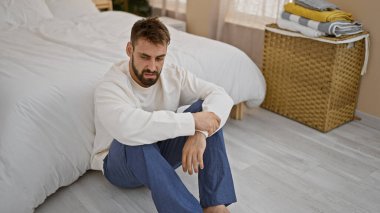 Stresli, genç, İspanyol bir adam, tamamen uyanık, evde tek başına oturuyor, baş ağrısı çekiyor. pijamalı depresif bir adam, battaniyenin altında, endişeli ve endişeli bir ifade.