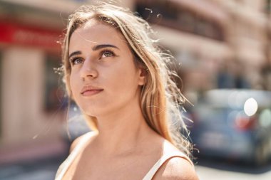 Sokakta ciddi bir ifadeyle gökyüzüne bakan genç sarışın kadın.