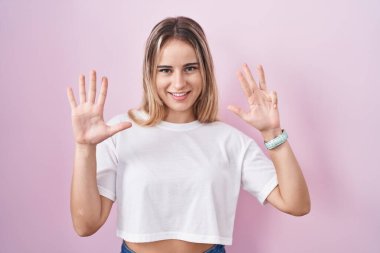 Pembe arka planda duran genç sarışın kadın dokuz numarayı gösterip işaret ederken kendinden emin ve mutlu bir şekilde gülümsüyor.. 