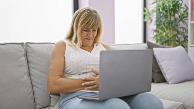 Karnı ağrıyan sarışın, orta yaşlı bir kadının dizüstü bilgisayarını evde yorucu bir çileye çeviriyor..