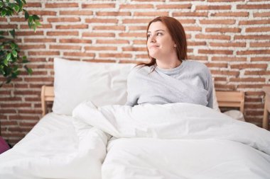 Young beautiful plus size woman smiling confident sitting on bed at bedroom